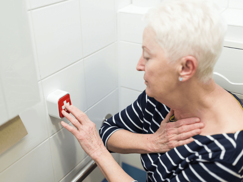Klientka domova seniorů stiskává tísňové tlačítko HelpLivi na zdi koupelny